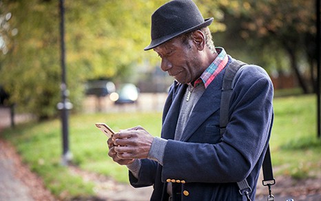 An older man standing outside looking at his smartphone