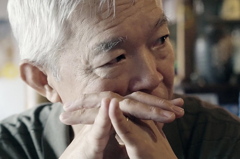 An elderly man leans his face against his hands, looking sideways, off into the distance, and concerned