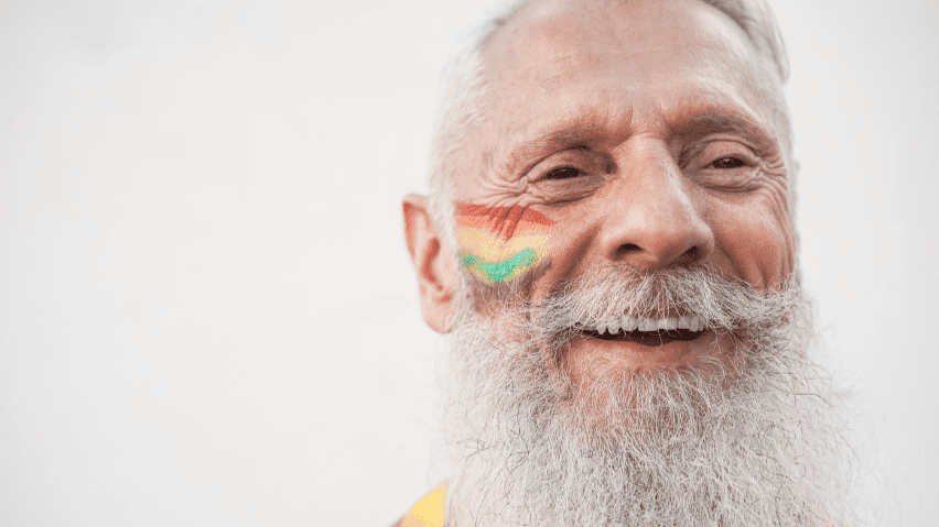 Happy senior man smiling with pride flag painted on face.